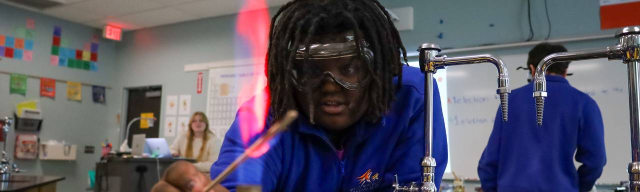 A high school boy holds material into a lit Bunsen burner during science class experiements